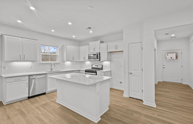 kitchen featuring white cabinets, appliances with stainless steel finishes, a center island, light countertops, and a sink