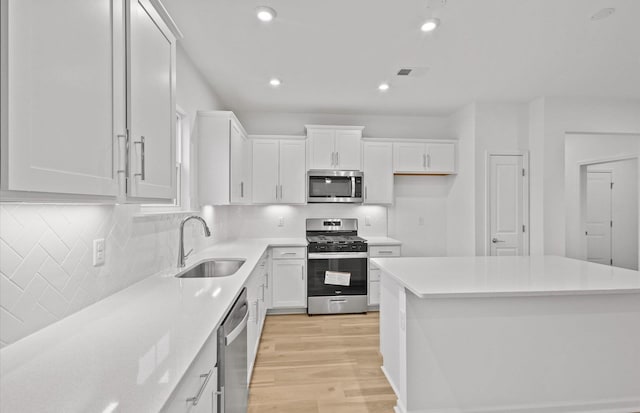 kitchen featuring light wood finished floors, a kitchen island, stainless steel appliances, white cabinetry, and a sink