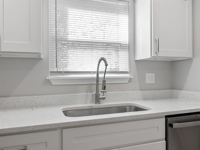 kitchen with white cabinets, a sink, stainless steel dishwasher, and light stone countertops