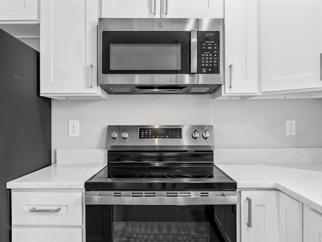 kitchen with stainless steel appliances, white cabinets, and light stone countertops