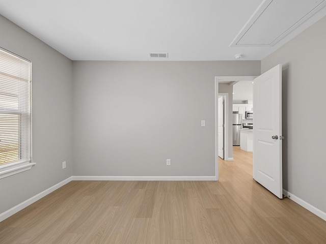 empty room featuring baseboards, attic access, visible vents, and light wood-style floors