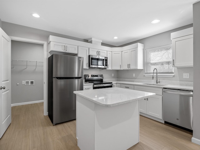 kitchen featuring light wood finished floors, a kitchen island, appliances with stainless steel finishes, white cabinetry, and a sink