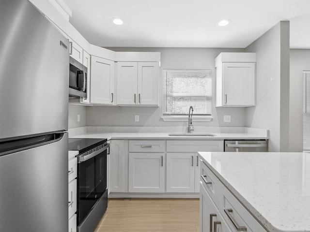 kitchen featuring light stone countertops, white cabinetry, appliances with stainless steel finishes, and a sink