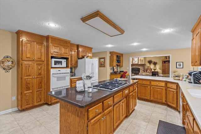 kitchen featuring brown cabinets, a fireplace, a kitchen island, a textured ceiling, and white appliances