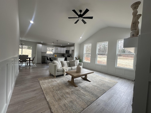 living room with light wood-type flooring, recessed lighting, vaulted ceiling, and a decorative wall