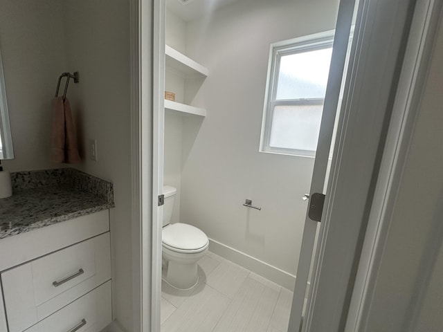 half bath featuring baseboards, vanity, toilet, and tile patterned floors