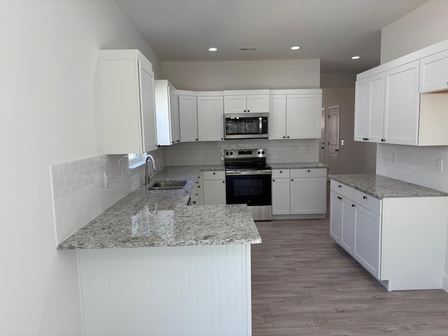 kitchen featuring light wood finished floors, appliances with stainless steel finishes, white cabinetry, a sink, and a peninsula