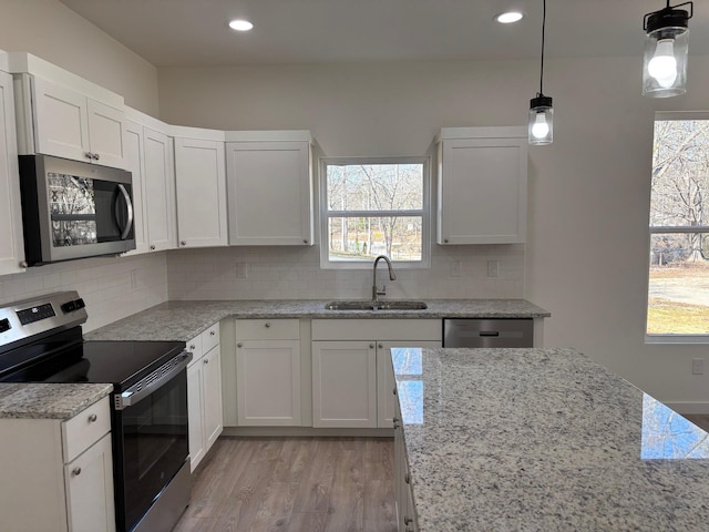 kitchen with a sink, white cabinetry, hanging light fixtures, appliances with stainless steel finishes, and decorative backsplash