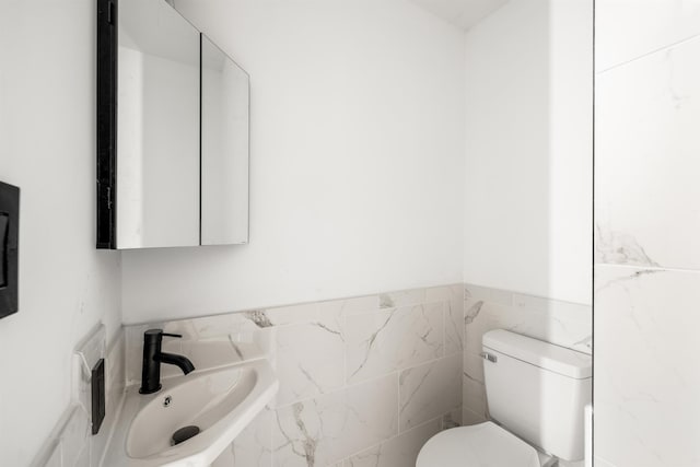 bathroom with toilet, tile walls, and a sink