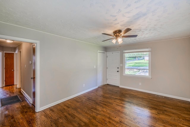 empty room featuring dark wood-type flooring, attic access, a ceiling fan, a textured ceiling, and baseboards