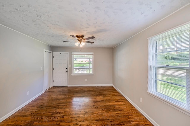 spare room with baseboards, dark wood finished floors, a ceiling fan, crown molding, and a textured ceiling