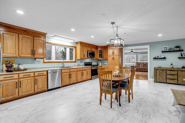 kitchen with stainless steel appliances, a sink, hanging light fixtures, light countertops, and glass insert cabinets