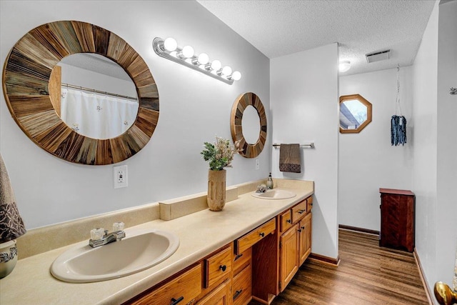 bathroom with wood finished floors, a sink, a textured ceiling, and double vanity