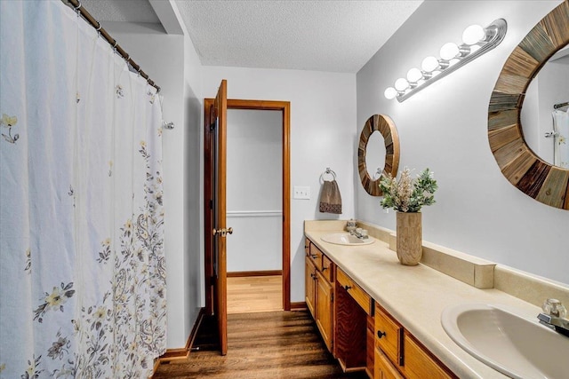 bathroom featuring double vanity, a textured ceiling, a sink, and wood finished floors