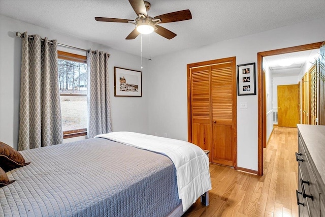 bedroom featuring a closet, light wood-style flooring, ceiling fan, a textured ceiling, and baseboards