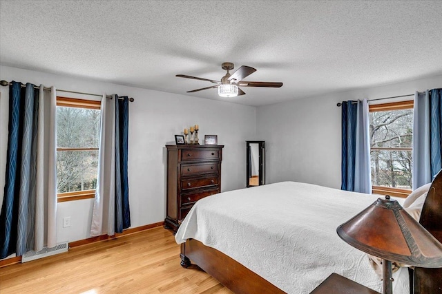 bedroom with light wood finished floors, ceiling fan, multiple windows, and visible vents