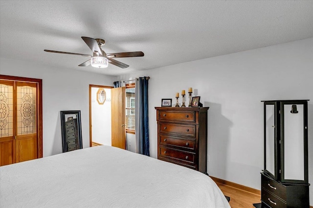 bedroom with a textured ceiling, light wood finished floors, a ceiling fan, and baseboards