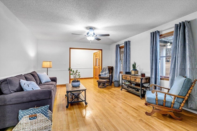 living area with a ceiling fan, a textured ceiling, baseboards, and wood finished floors