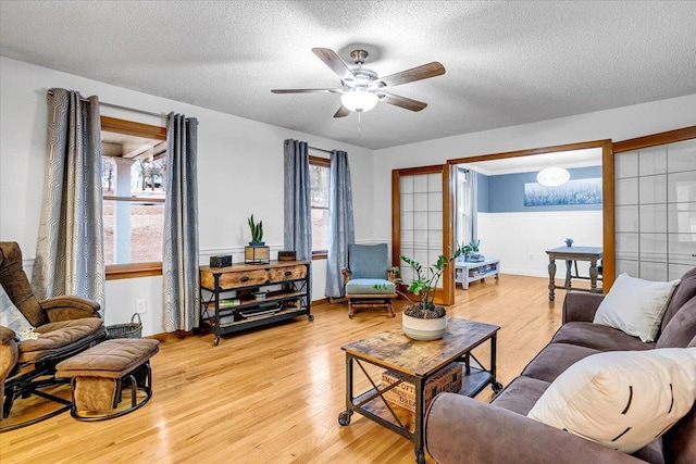 living room featuring light wood-type flooring, ceiling fan, and a textured ceiling