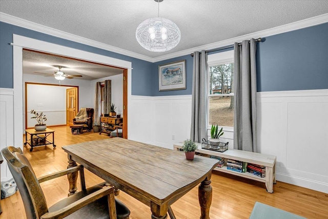 dining room with wainscoting, crown molding, a textured ceiling, and light wood finished floors