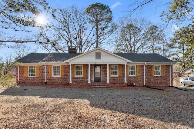 ranch-style home featuring a chimney, a porch, and brick siding