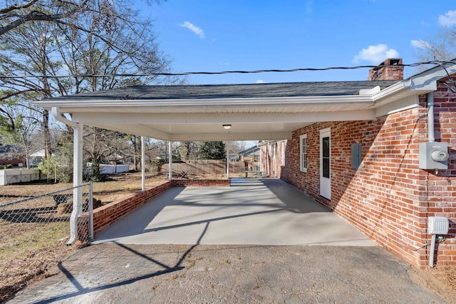 view of parking / parking lot featuring an attached carport, driveway, and fence