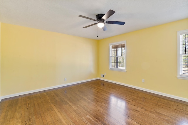 unfurnished room featuring visible vents, wood finished floors, a ceiling fan, and baseboards