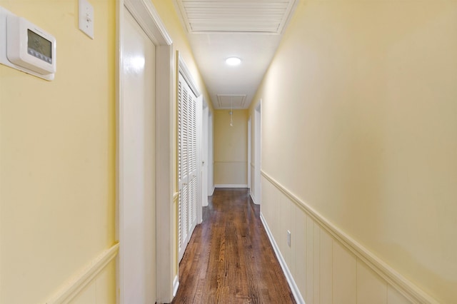 hallway with attic access, visible vents, dark wood-type flooring, and wainscoting