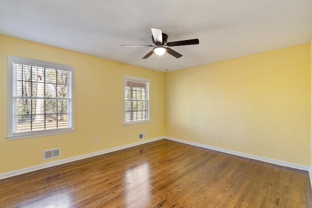 spare room with wood finished floors, visible vents, and baseboards