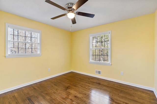 empty room featuring a ceiling fan, visible vents, baseboards, and wood finished floors