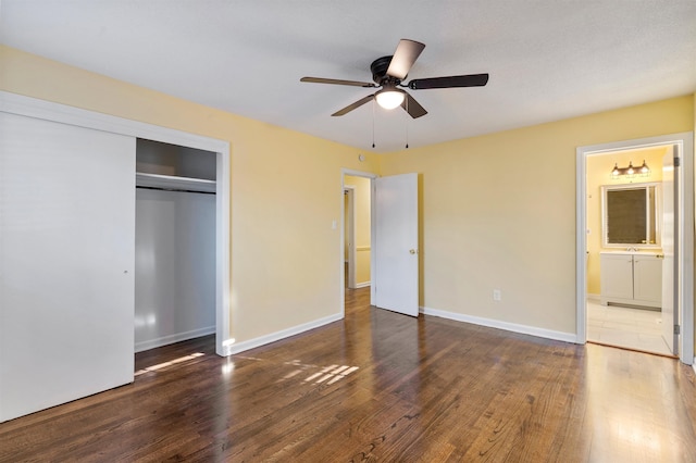 unfurnished bedroom with dark wood-style flooring, a ceiling fan, baseboards, a closet, and ensuite bath