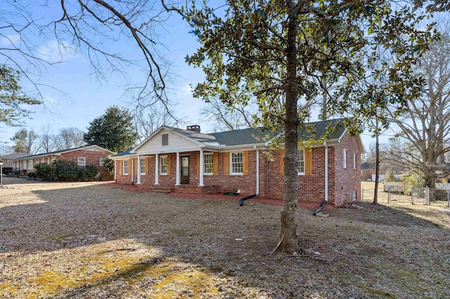 view of front facade with brick siding, a chimney, and fence