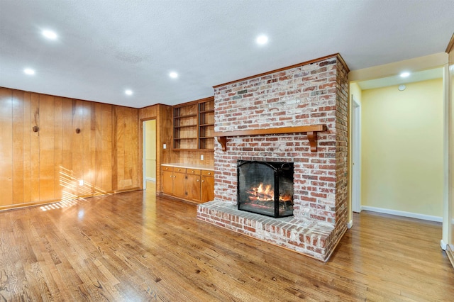 unfurnished living room with a textured ceiling, wooden walls, baseboards, light wood-type flooring, and a brick fireplace