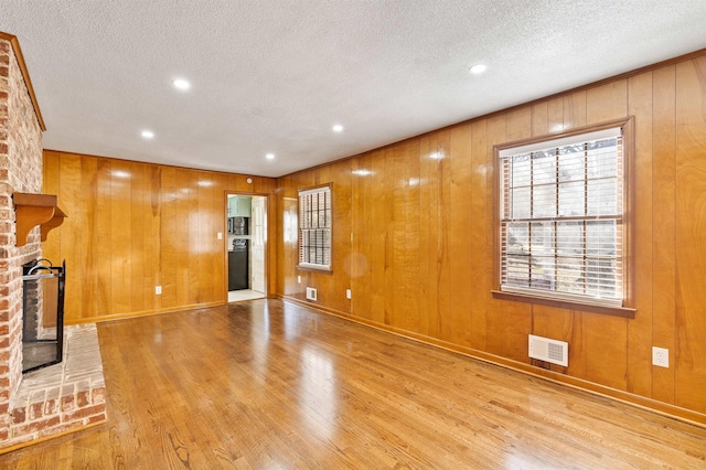 unfurnished living room with light wood-style floors, visible vents, a fireplace, and a textured ceiling