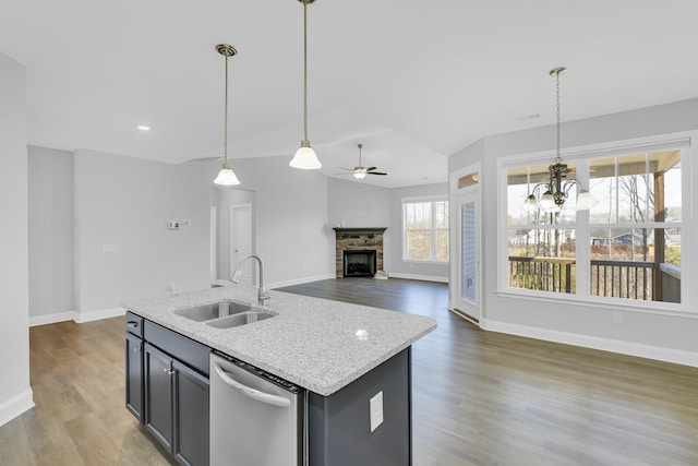 kitchen with a kitchen island with sink, a fireplace, a sink, light stone countertops, and dishwasher