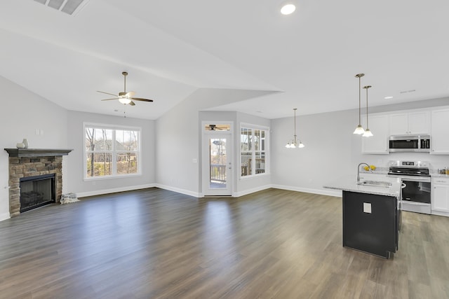 kitchen with stainless steel appliances, a sink, white cabinetry, open floor plan, and light stone countertops