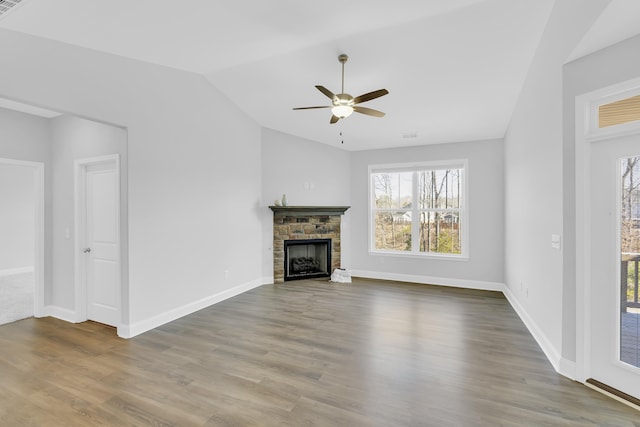 unfurnished living room with lofted ceiling, ceiling fan, a stone fireplace, wood finished floors, and baseboards