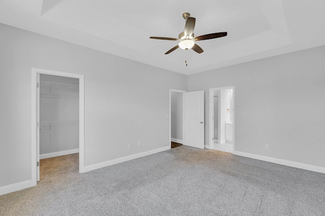 unfurnished bedroom featuring a raised ceiling, carpet flooring, a walk in closet, and baseboards