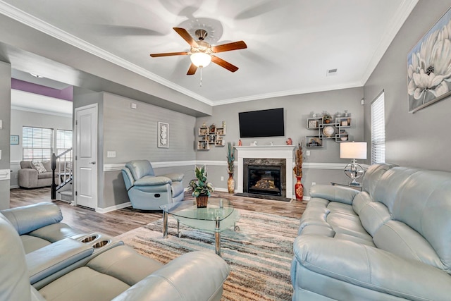 living room with baseboards, a ceiling fan, ornamental molding, light wood-style floors, and a high end fireplace