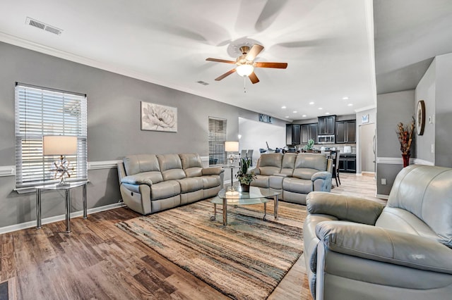 living room with baseboards, visible vents, a ceiling fan, wood finished floors, and crown molding