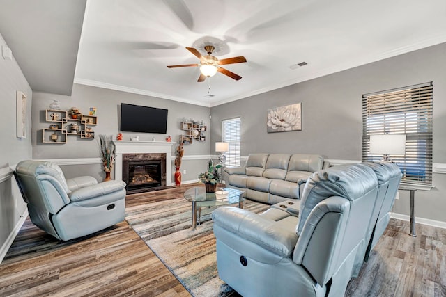 living area with crown molding, a fireplace, visible vents, and wood finished floors