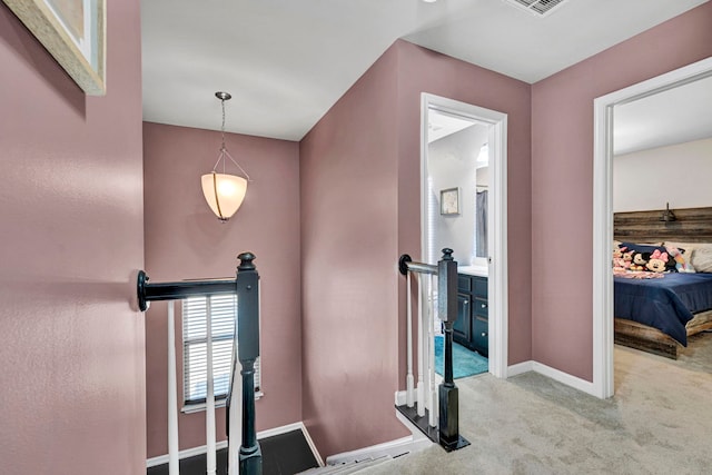 hallway with baseboards, light carpet, visible vents, and an upstairs landing