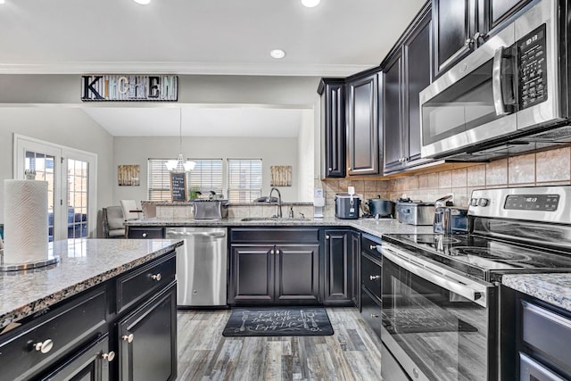 kitchen featuring stainless steel appliances, light stone counters, a sink, and decorative light fixtures