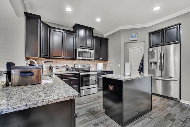 kitchen with light stone counters, appliances with stainless steel finishes, ornamental molding, a center island, and tasteful backsplash