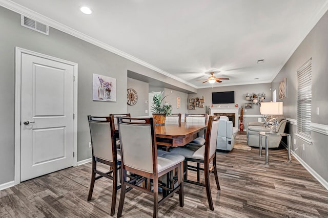 dining area featuring dark wood-style flooring, a fireplace, visible vents, a ceiling fan, and ornamental molding