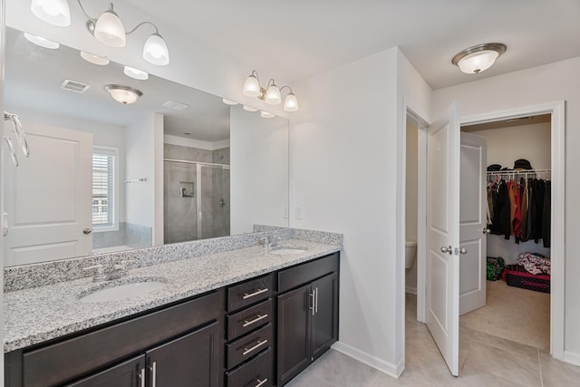 bathroom featuring a stall shower, visible vents, a walk in closet, and a sink