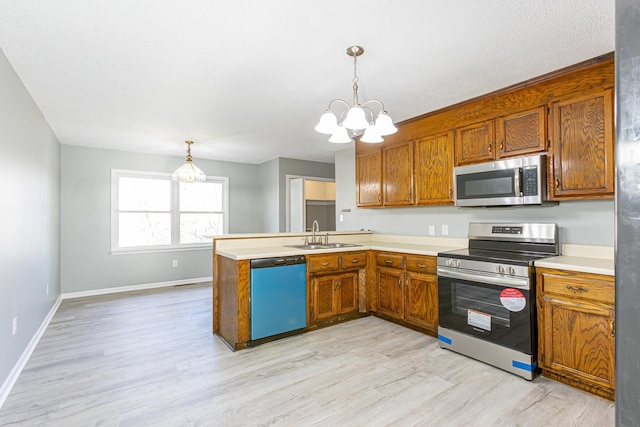 kitchen with decorative light fixtures, a peninsula, stainless steel appliances, light countertops, and a sink