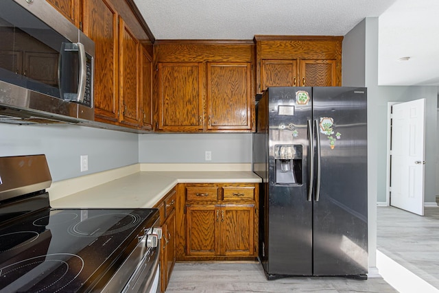 kitchen featuring a textured ceiling, stainless steel appliances, brown cabinetry, and light countertops