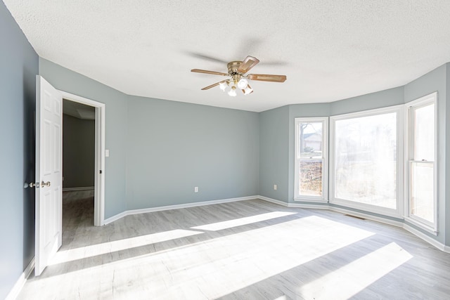 spare room featuring light wood-type flooring, a textured ceiling, and baseboards