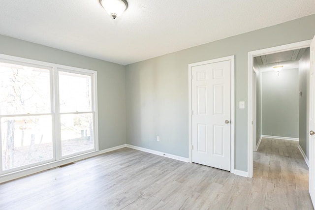 unfurnished bedroom featuring attic access, visible vents, baseboards, light wood-style flooring, and a textured ceiling